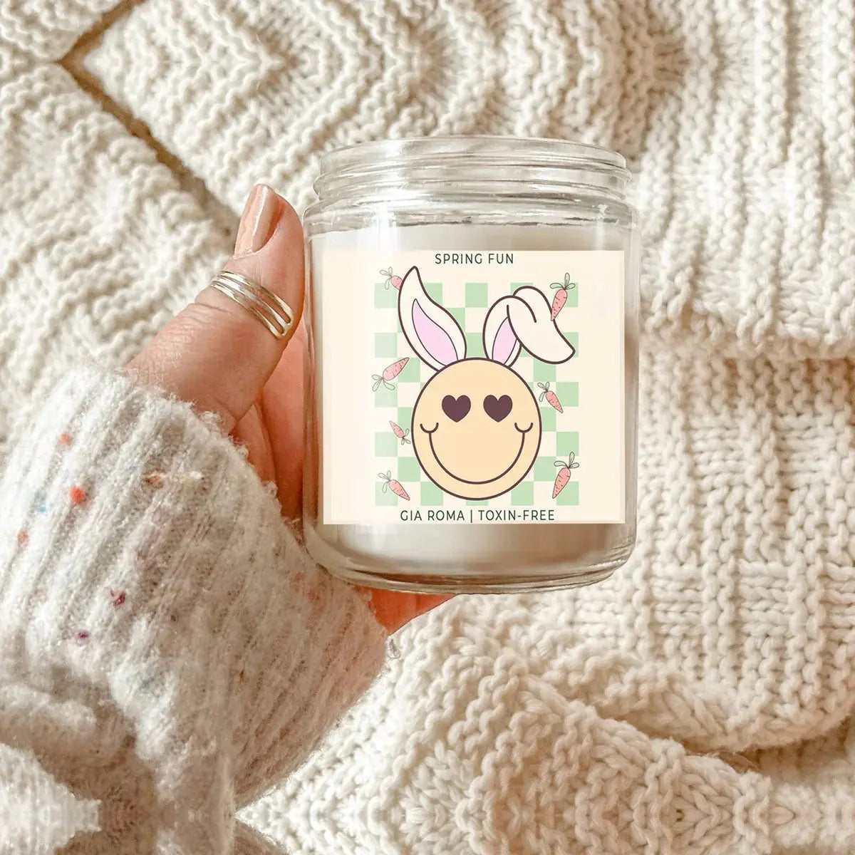 Candle with a bunny-themed label held by a person against a textured beige background