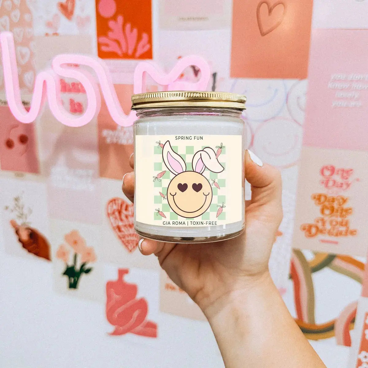 Hand holding a candle jar with a decorative label against a colorful background