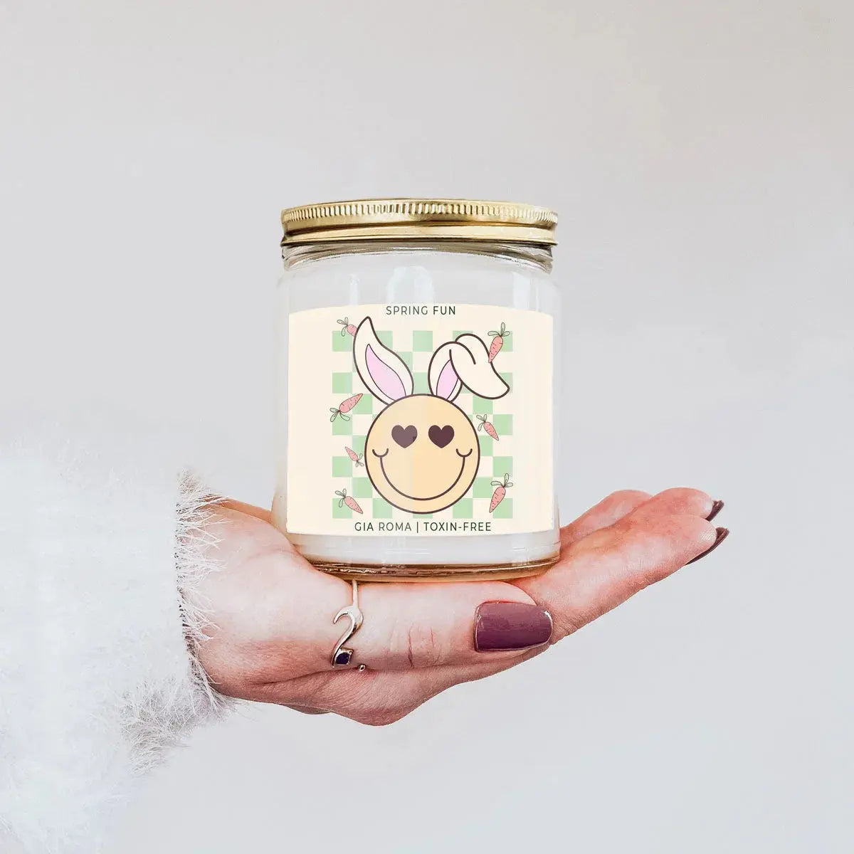 Hand holding a candle with a bunny design label against a white background