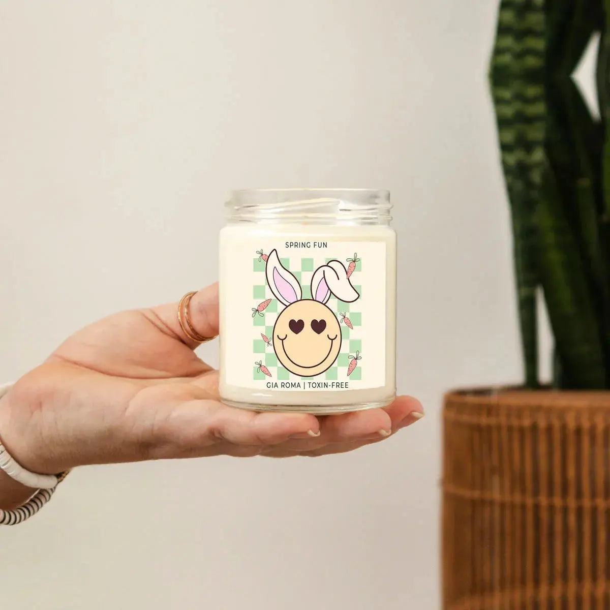 Hand holding a candle with a decorative label against a neutral background