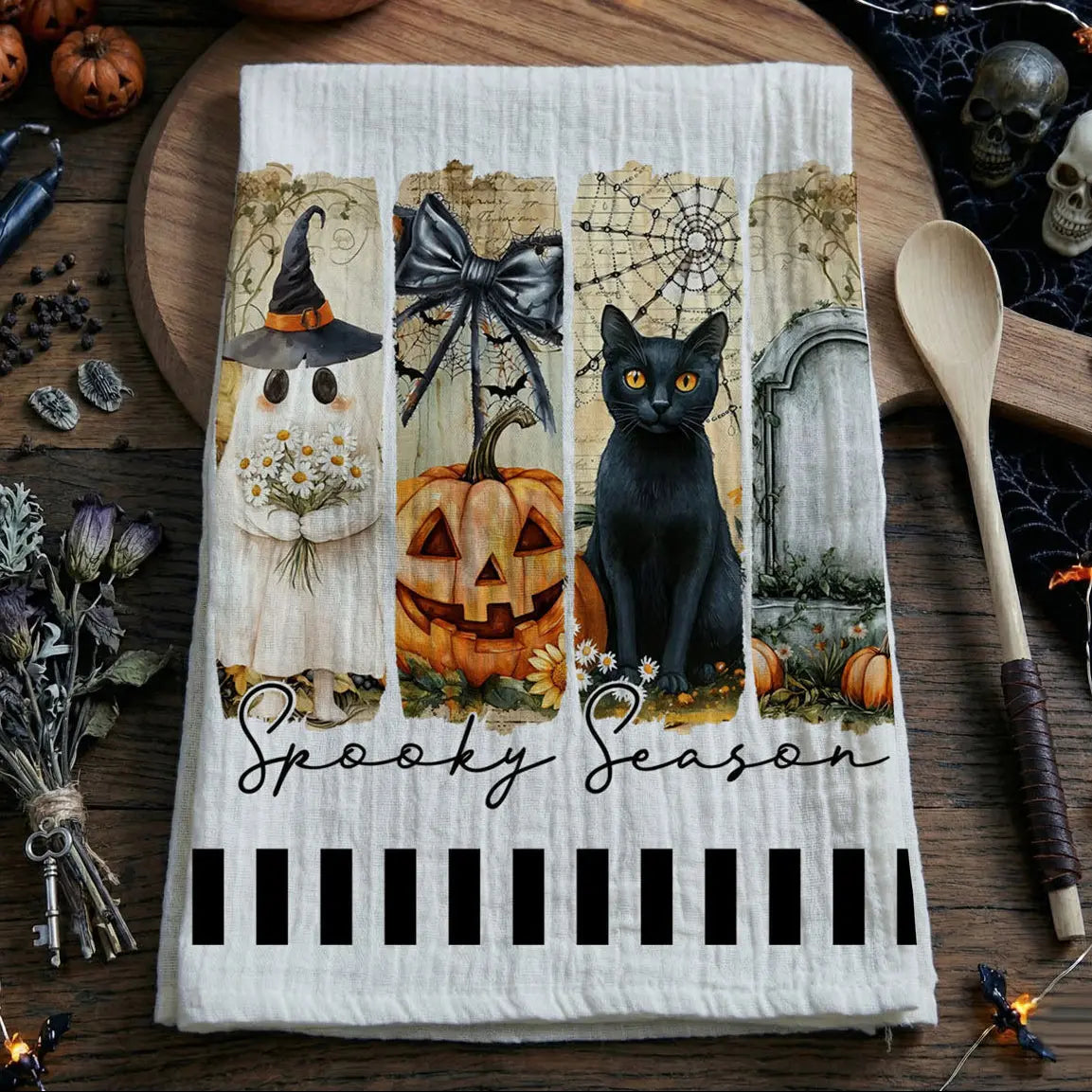 Halloween-themed kitchen towel with black cat, pumpkin, and ghost design on a wooden surface.