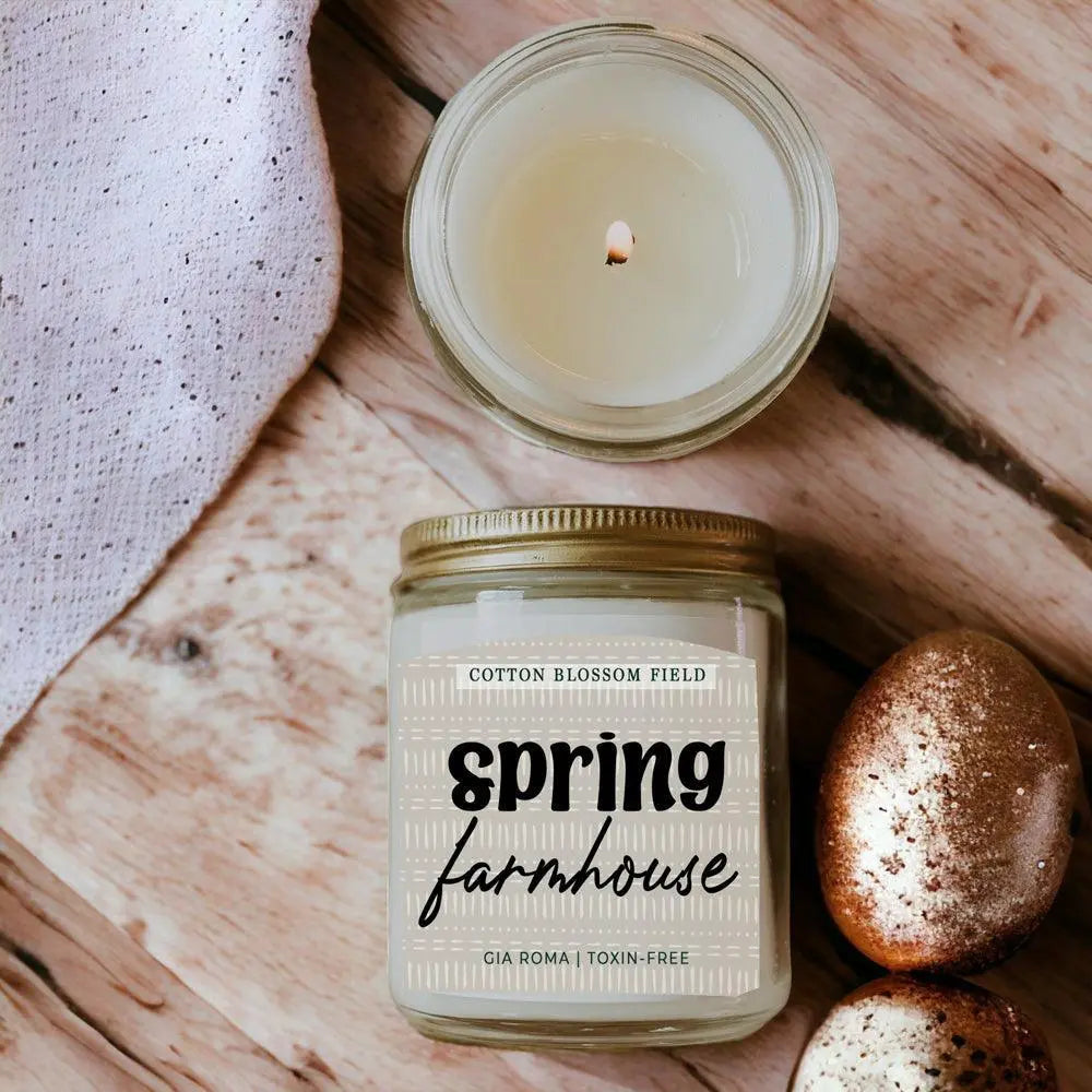 Candle jar labeled 'Spring Farmhouse' on a wooden surface with a cotton ball.