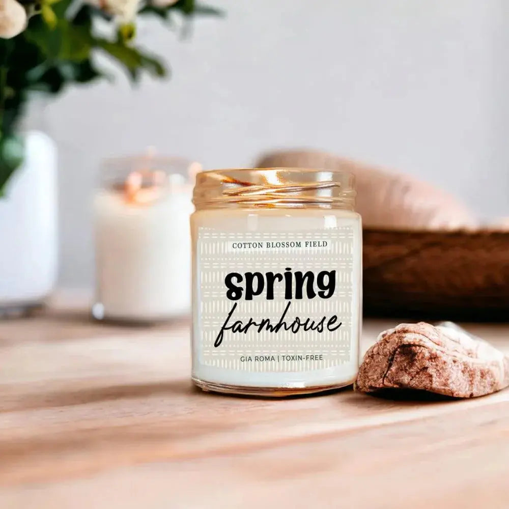 Candle labeled 'Spring Farmhouse' on a wooden surface with blurred background