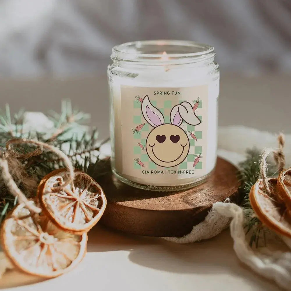 Candle in a glass jar with a decorative label on a wooden coaster, surrounded by Christmas decorations.