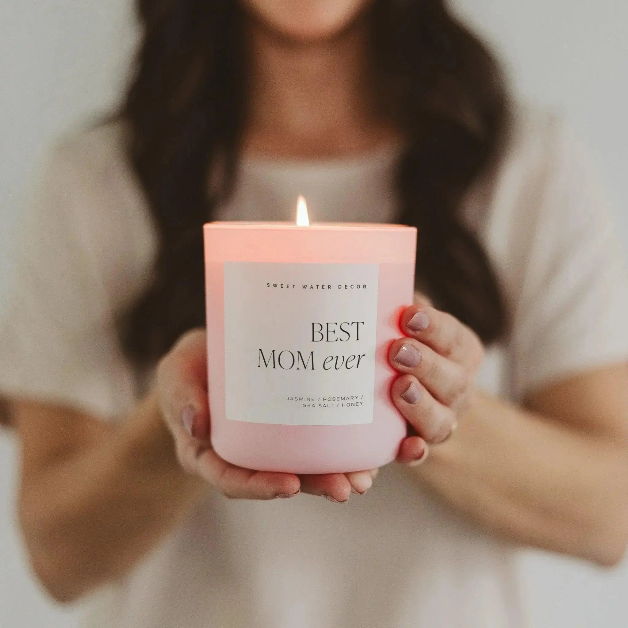 Pink 'Best Mom Ever' scented candle with jasmine, rosemary, sea salt & honey notes, held gently for cozy home decor.