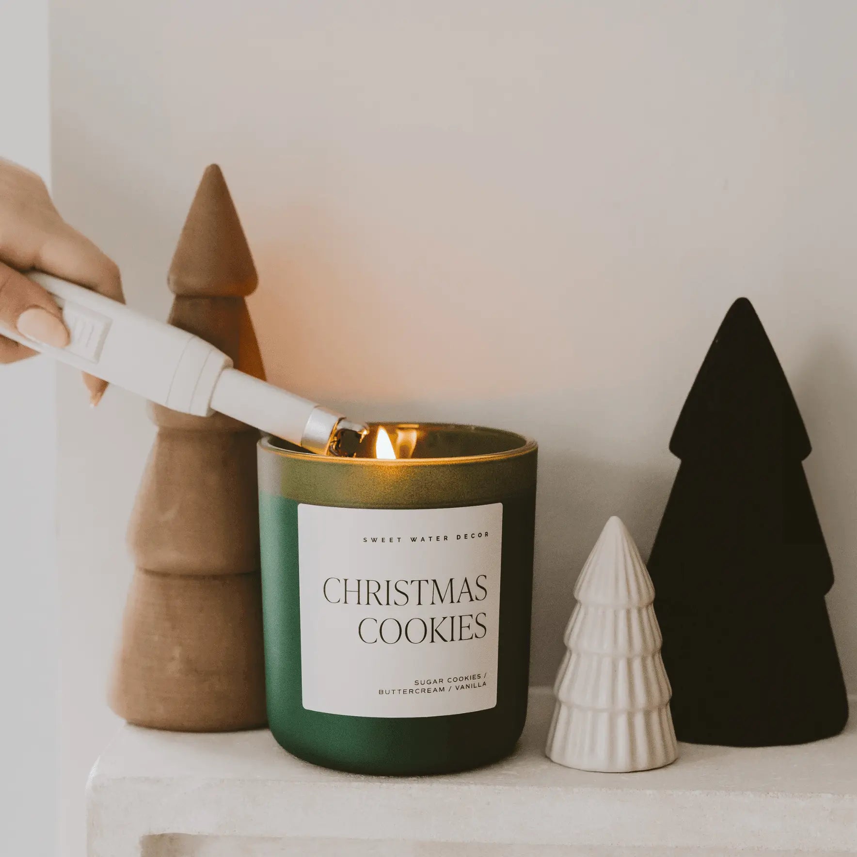 Candle labeled 'Christmas Cookies' being lit with decorative trees in the background