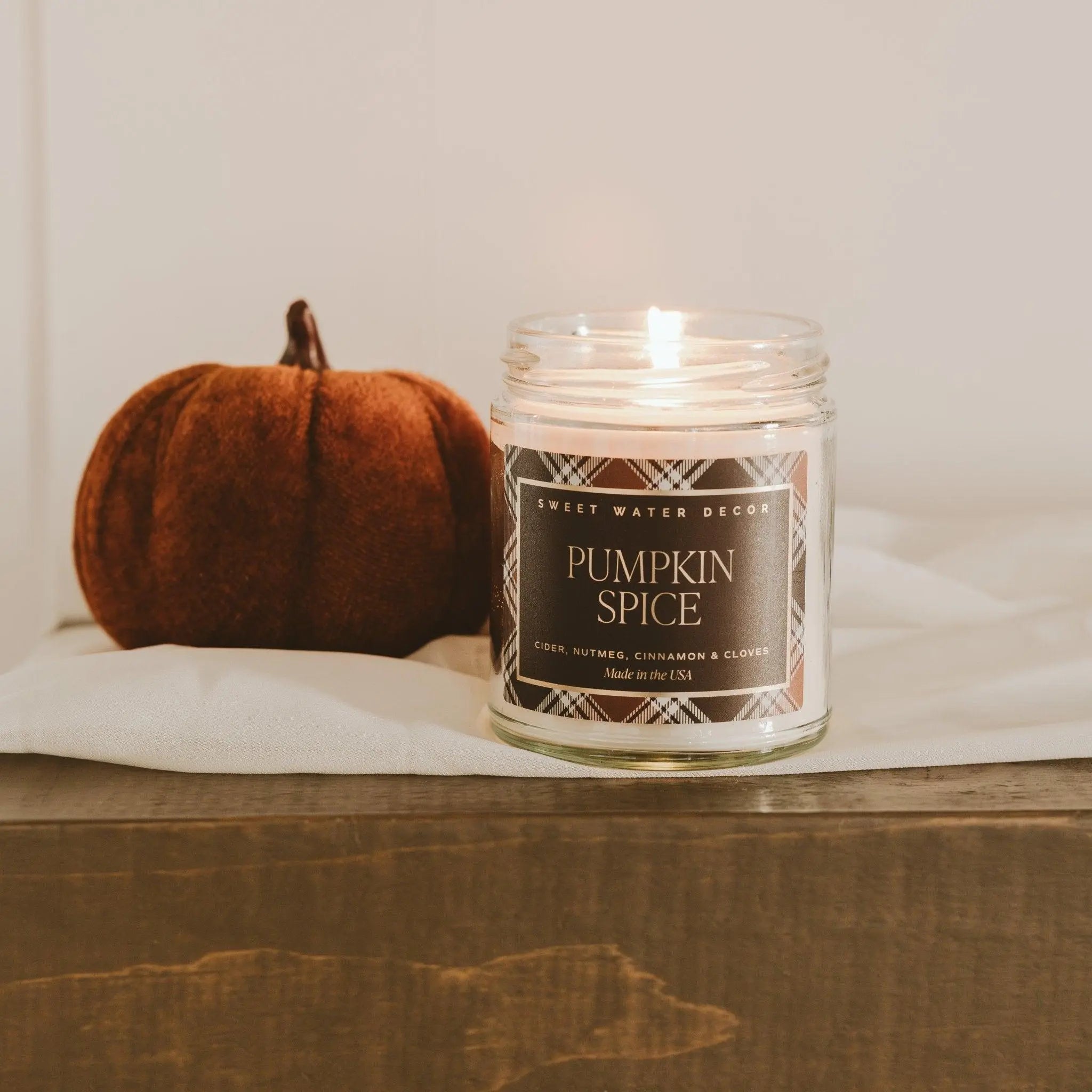Candle labeled 'Pumpkin Spice' next to a small pumpkin on a wooden surface.
