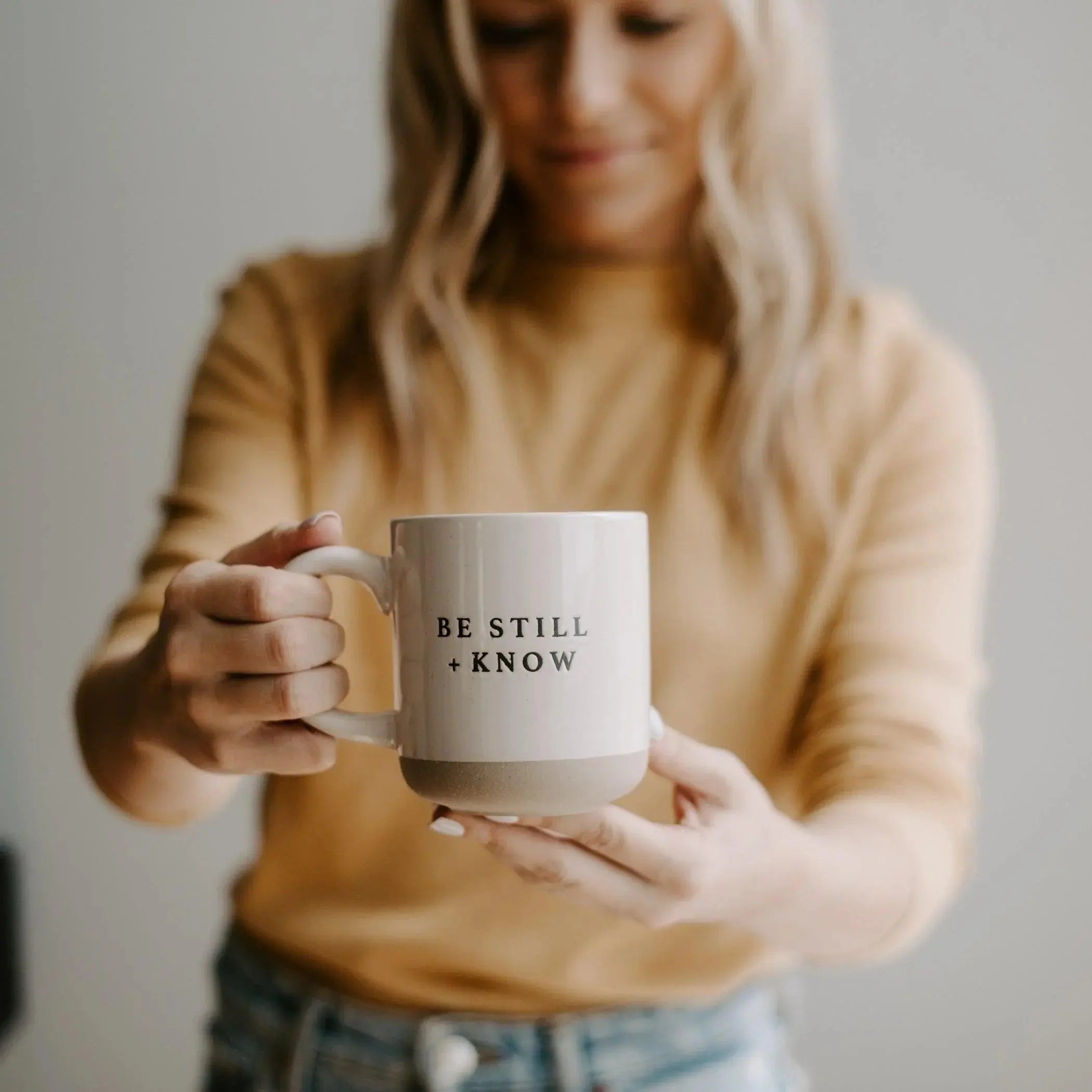 Woman holding cozy ceramic mug with 'Be Still + Know' quote, farmhouse home decor
