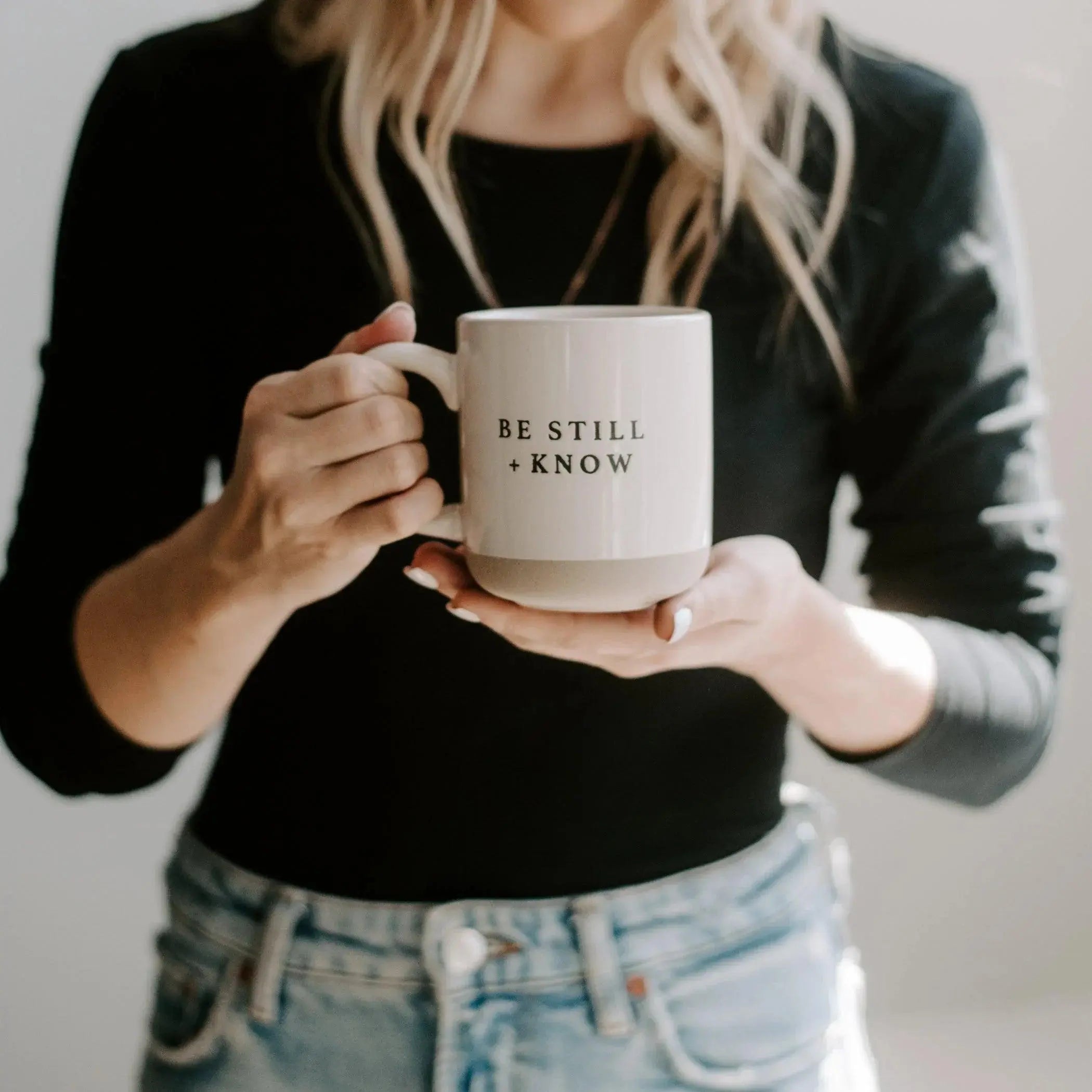 Woman holding cozy ceramic mug with 'Be Still + Know' text, farmhouse style home decor