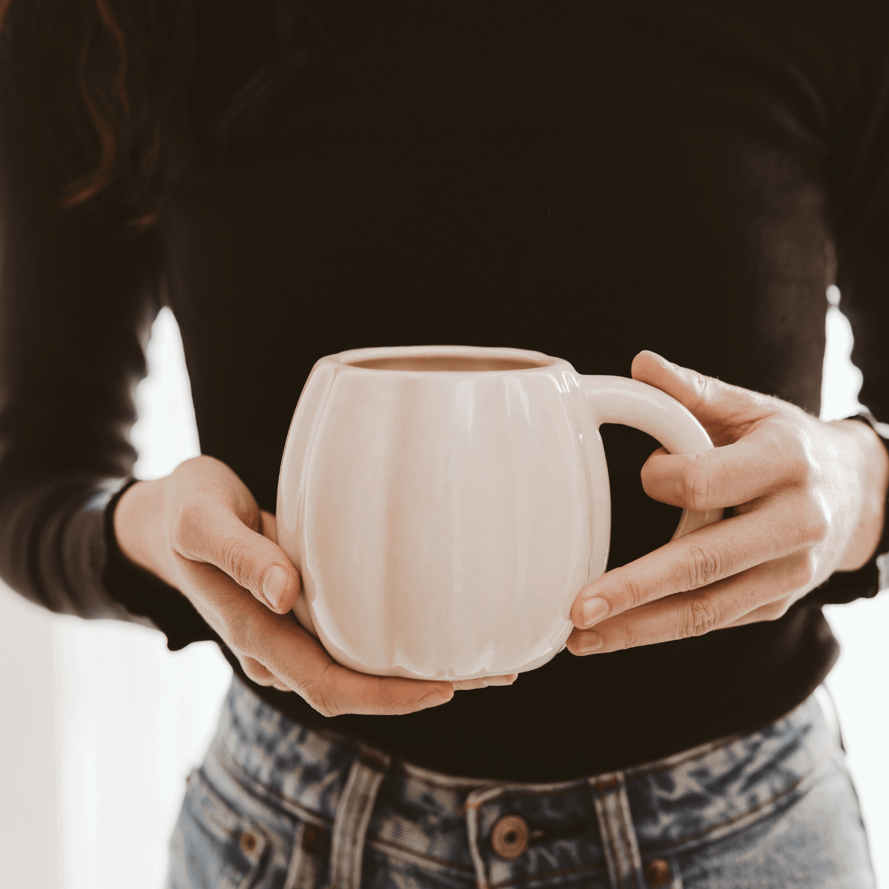 Person holding a white ceramic mug with a blurred background