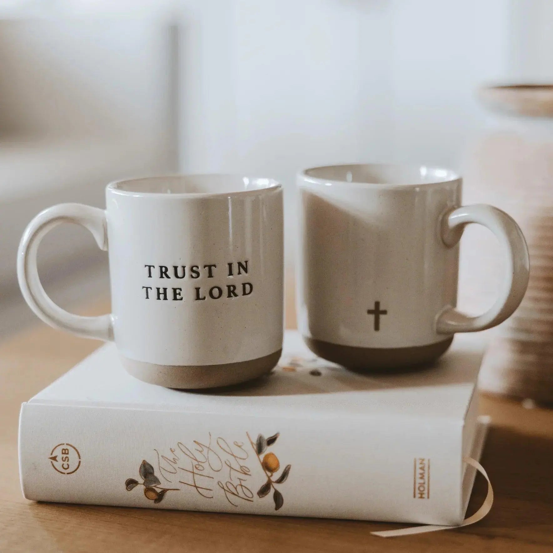 Faith-themed ceramic mugs with 'Trust in the Lord' and cross design, styled on a Bible for cozy home decor