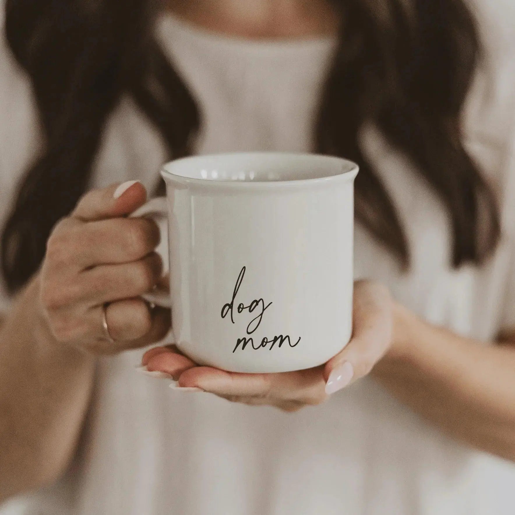 White ceramic mug with 'dog mom' text, held by woman in cozy farmhouse style
