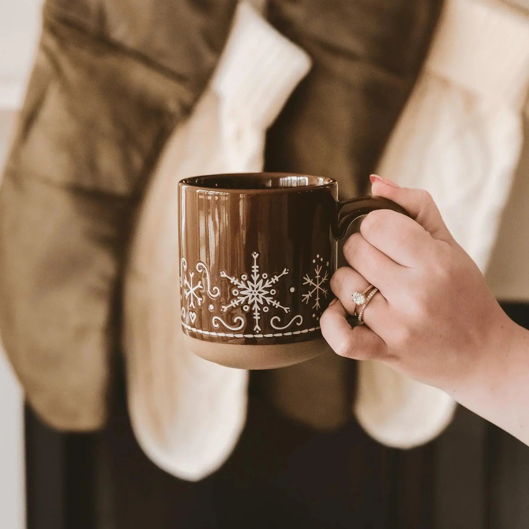 Cozy brown mug with white snowflake designs, held in hand near festive stockings, perfect for farmhouse winter decor.