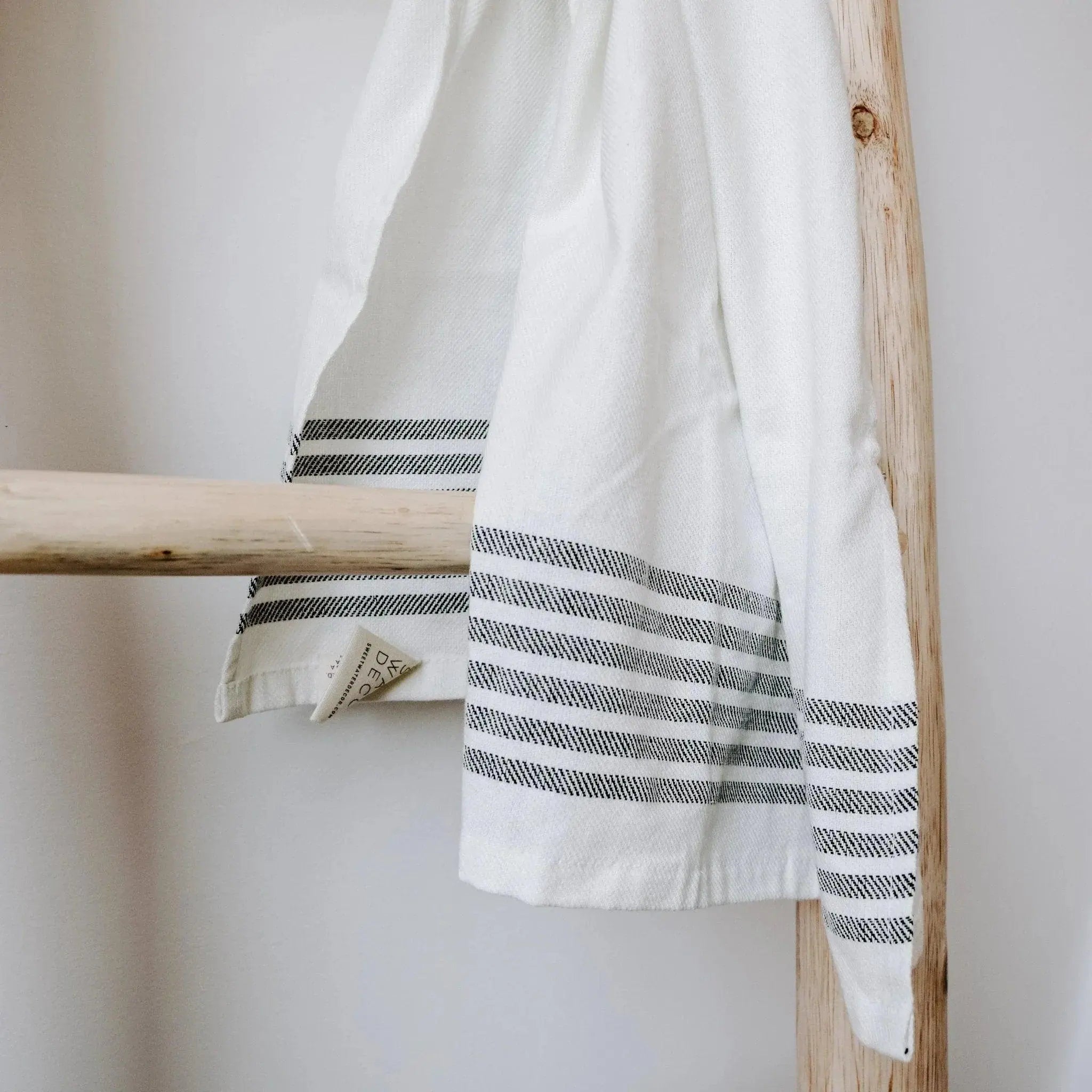 White farmhouse kitchen towel with black stripes hanging on wooden ladder, cozy cottage decor