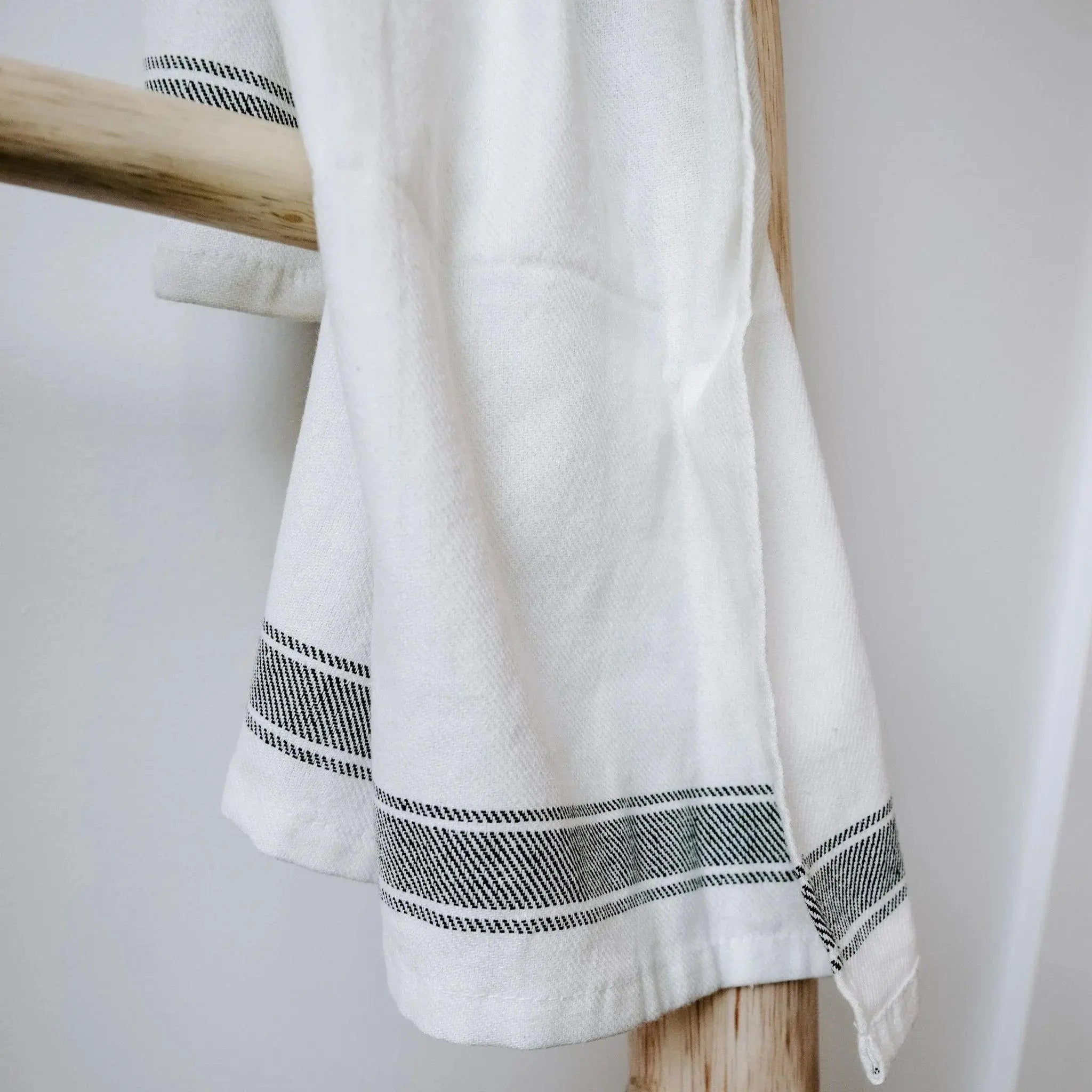 White farmhouse kitchen towel with black stripe pattern hanging on wooden rack