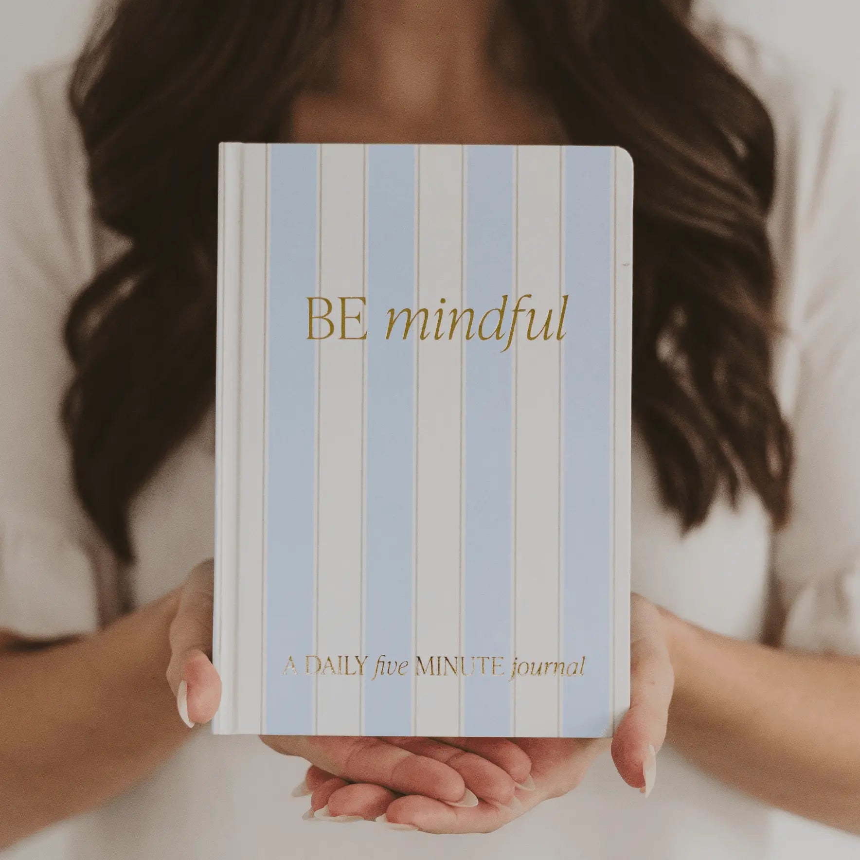 Person holding a striped journal with 'BE mindful' text