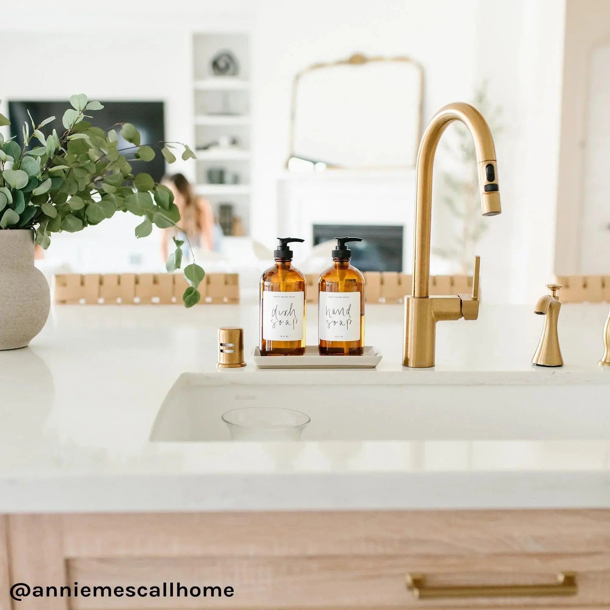Cozy kitchen sink with amber soap dispensers, gold faucet, and eucalyptus decor for farmhouse style home