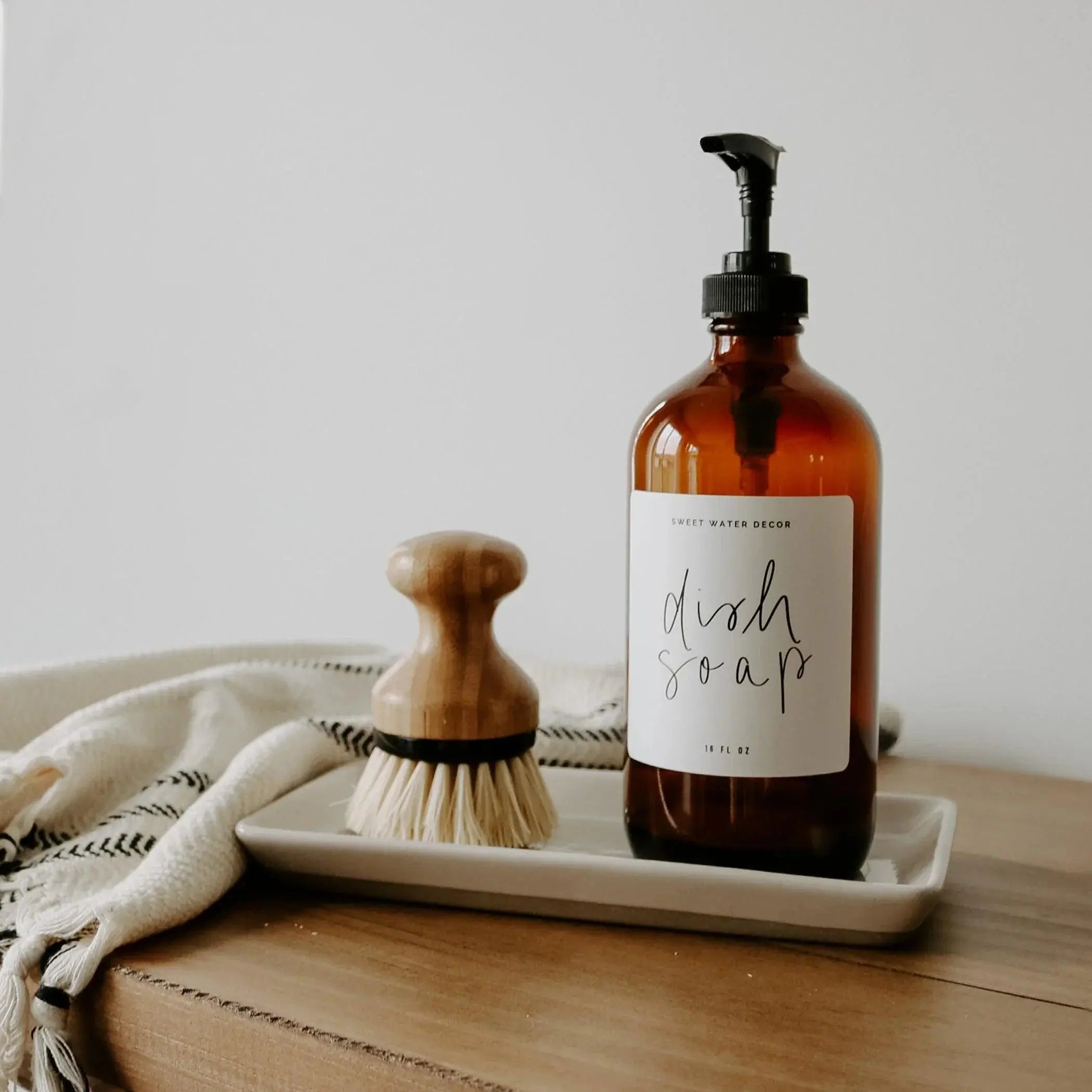 Amber glass dish soap bottle with wooden brush on ceramic tray, farmhouse kitchen decor