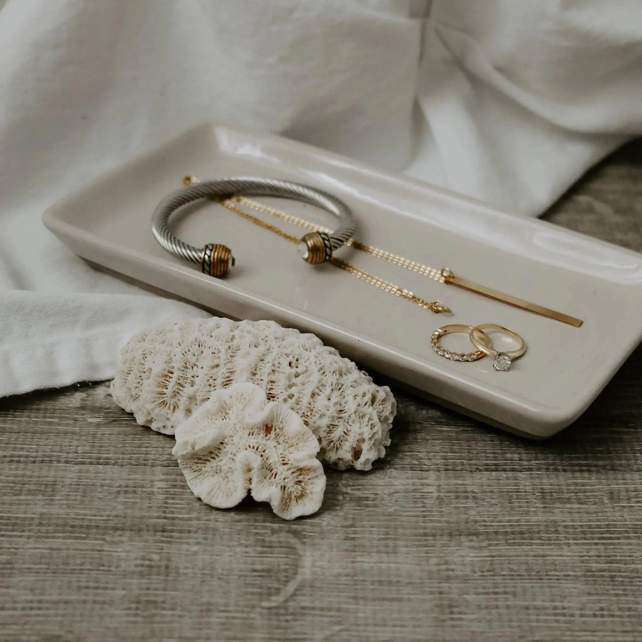 Ceramic jewelry tray with gold rings, bracelet, and coral decor on rustic wood, cozy farmhouse style