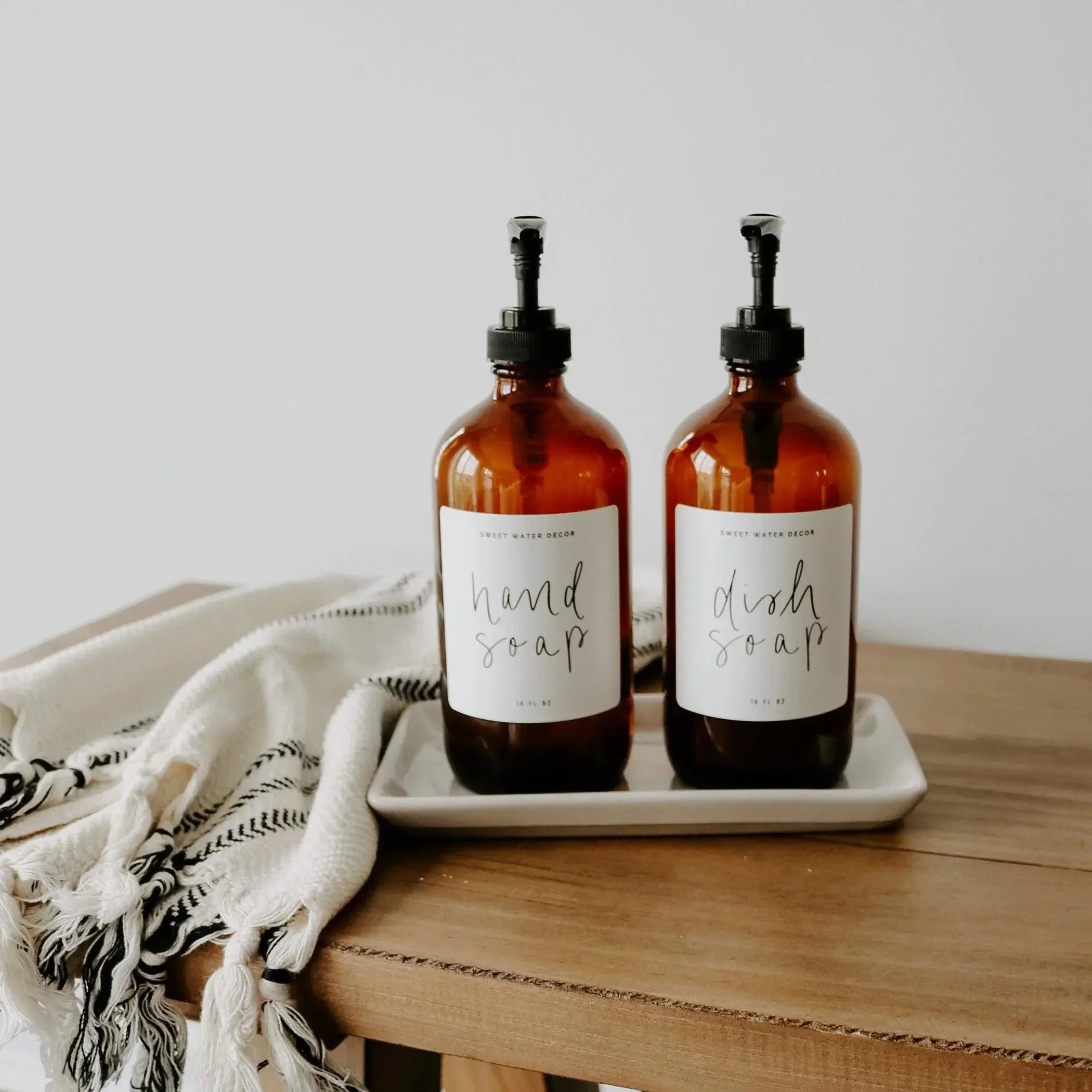 Amber glass hand soap and dish soap dispensers with farmhouse labels on wooden table, cozy home decor
