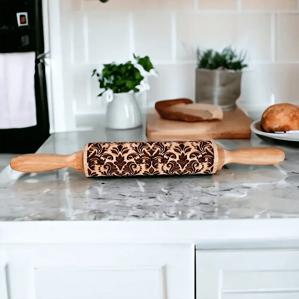 Decorative rolling pin on a kitchen counter with plants and a loaf of bread in the background.