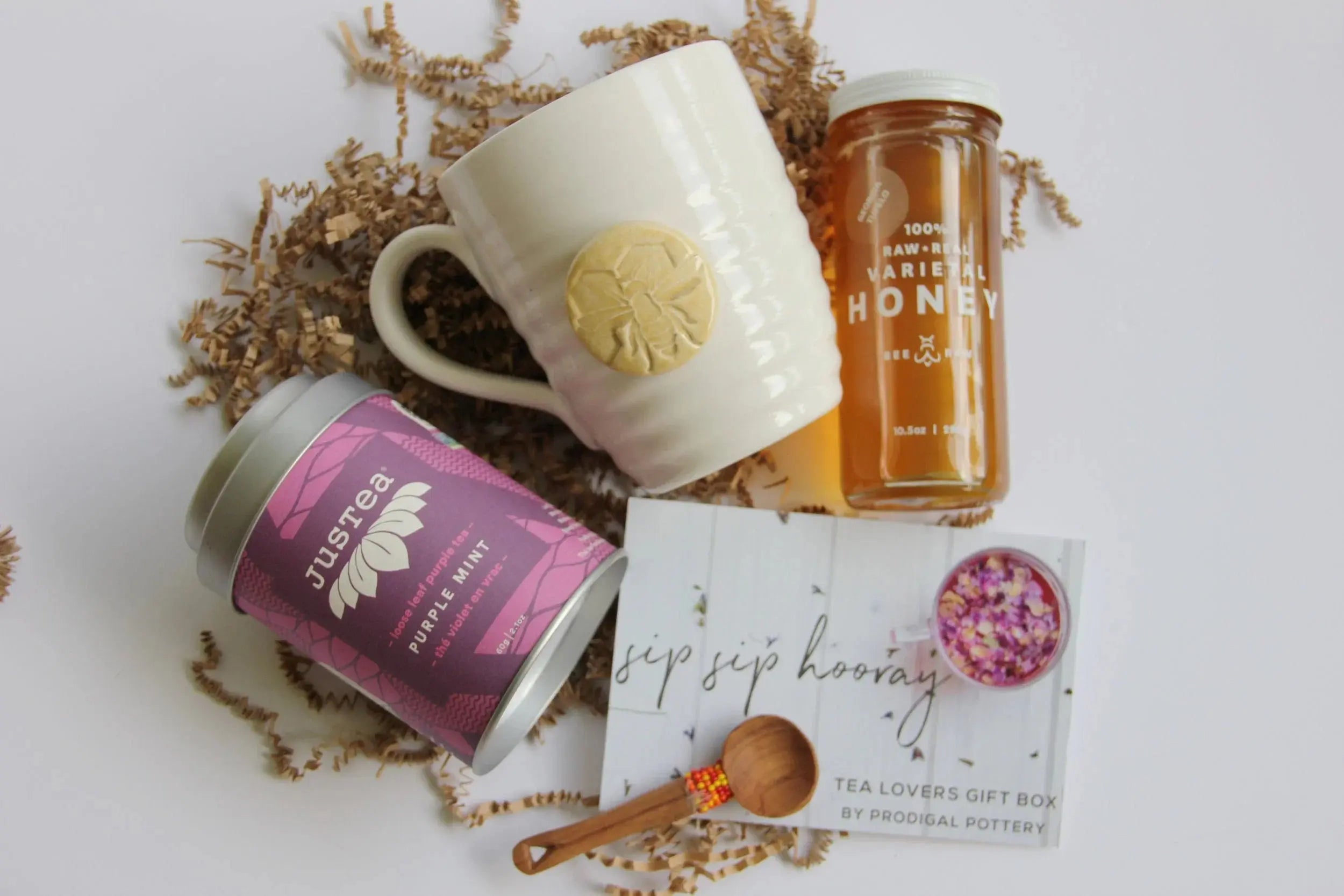 Tea lovers gift box with ceramic mug, raw honey, purple mint tea, and wooden spoon on shredded paper
