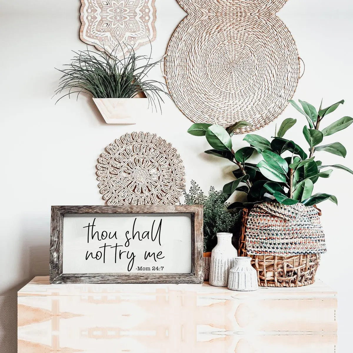 Decorative setup with plants, wicker baskets, and a framed quote on a wooden surface.