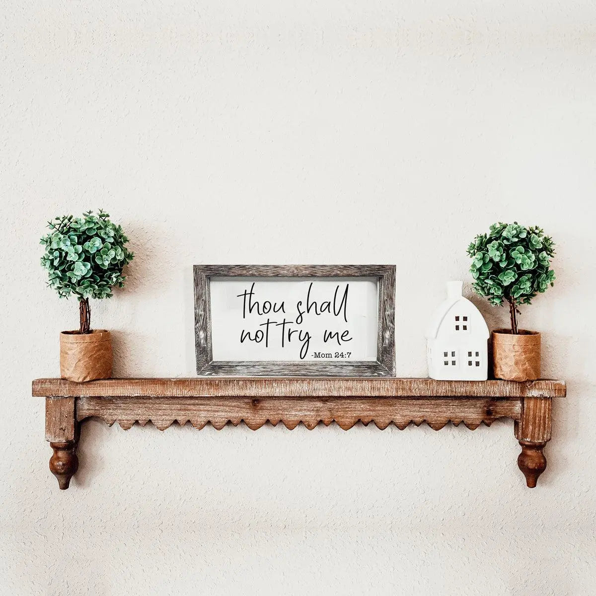 Wooden shelf with decorative items including potted plants and a framed quote on a plain wall.
