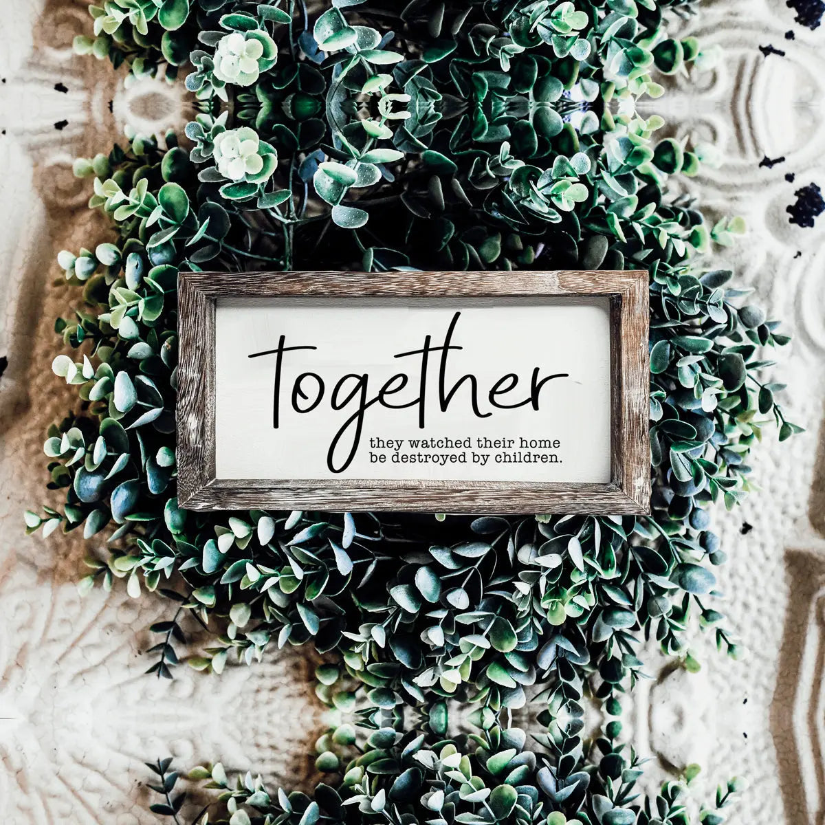 Wooden frame with 'Together' text surrounded by green foliage on a textured background