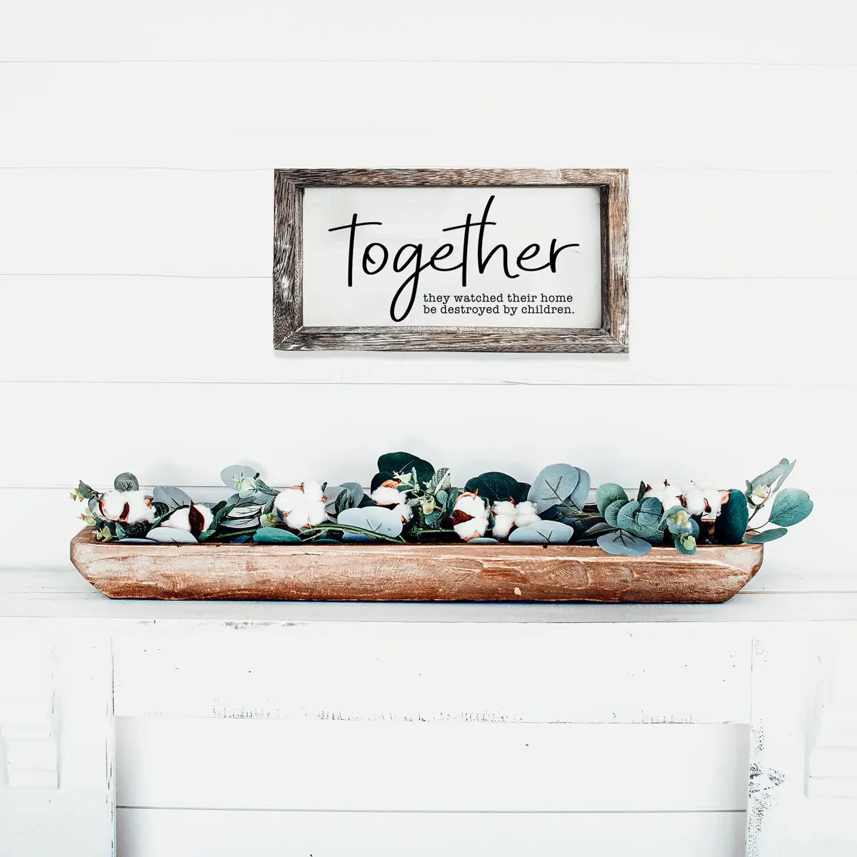 Decorative sign with 'Together' text above a wooden tray with greenery on a white surface.