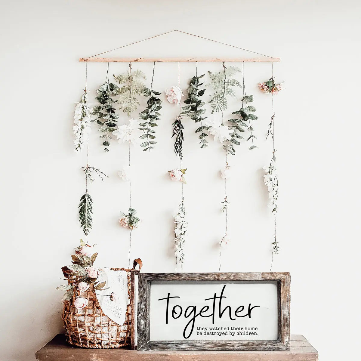 Decorative wall hanging with plants and a framed quote on a white background