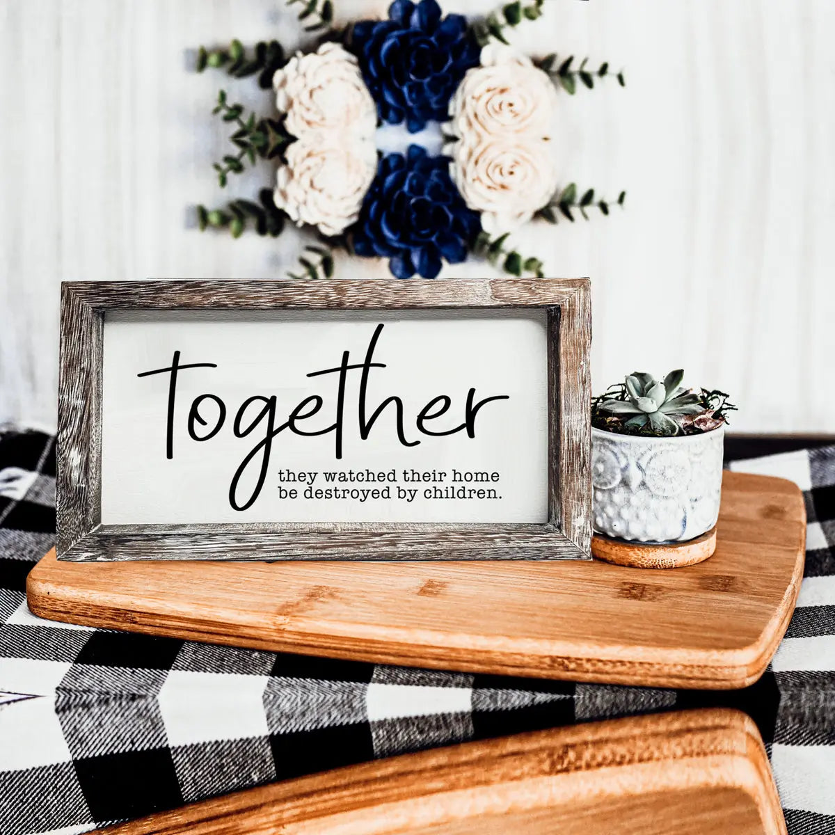 Framed sign with 'Together' text on a wooden surface with flowers in the background