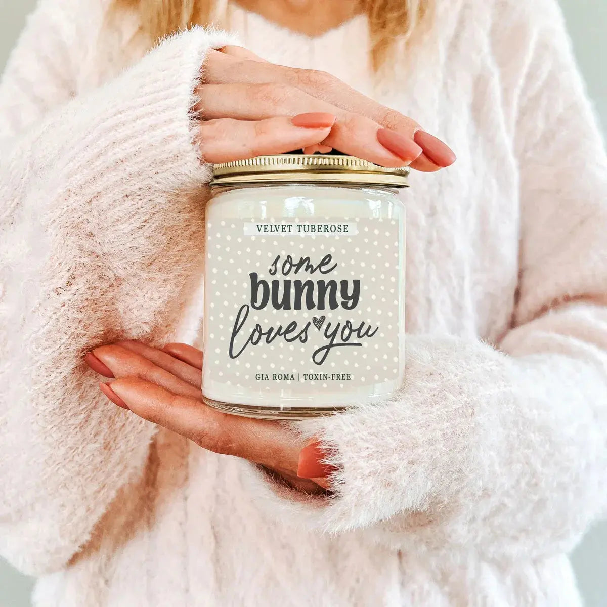 Person holding a candle labeled 'some bunny loves you' with a soft pink background