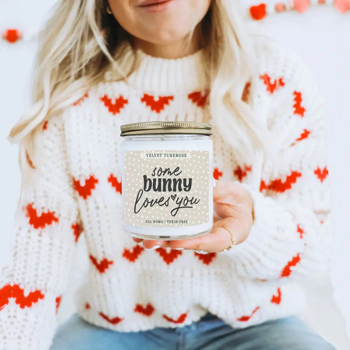 Person wearing a white sweater with red patterns, holding a candle labeled 'Spring Cookies for Peeps Sake'.