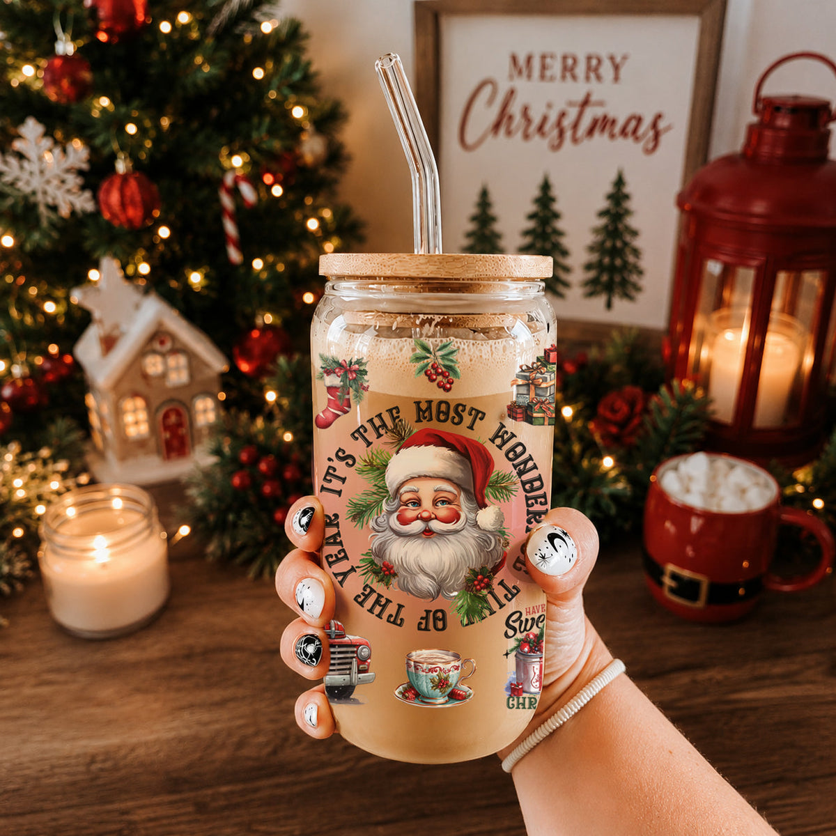 Hand holding a Christmas-themed tumbler with Santa Claus design in front of a decorated Christmas tree.