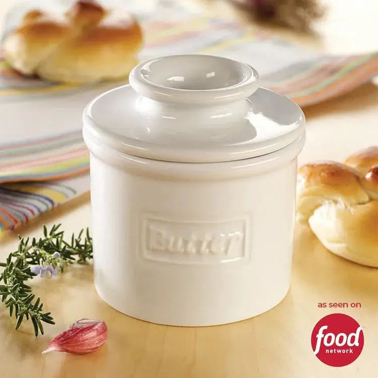 White ceramic butter crock with lid, farmhouse kitchen decor, fresh bread and herbs nearby
