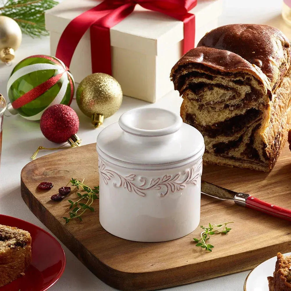 White ceramic jar with leaf design on wooden board, holiday ornaments, and cinnamon swirl bread nearby