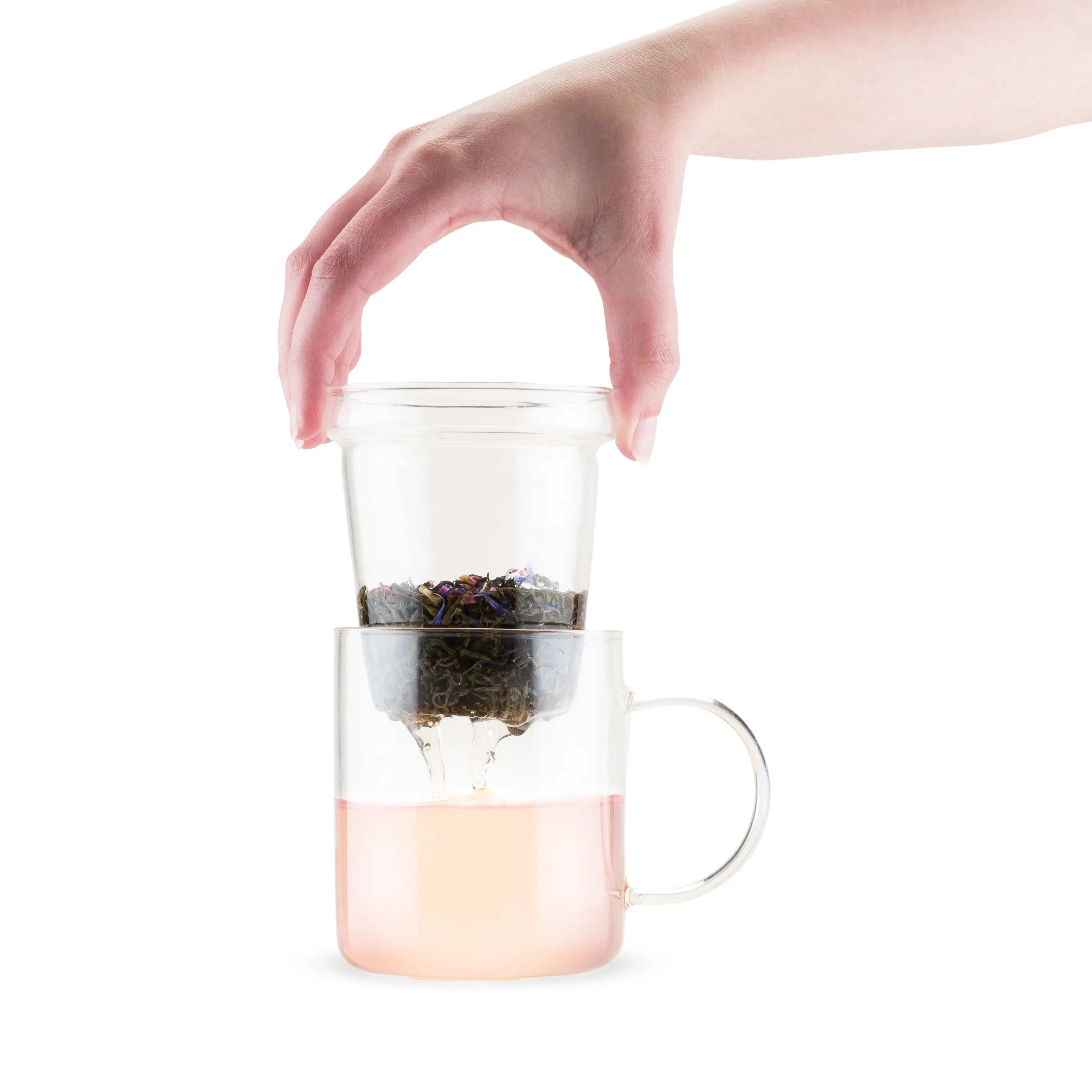 Clear glass tea infuser with pink base held by a hand on a white background