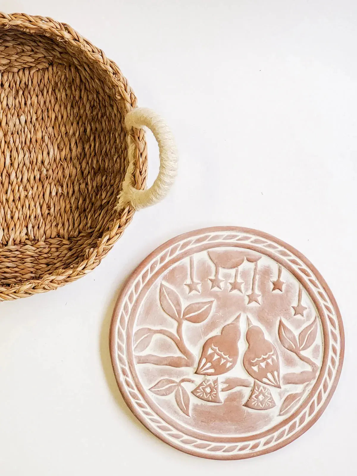 Woven seagrass basket with rope handle beside rustic ceramic plate featuring embossed birds and stars, farmhouse decor