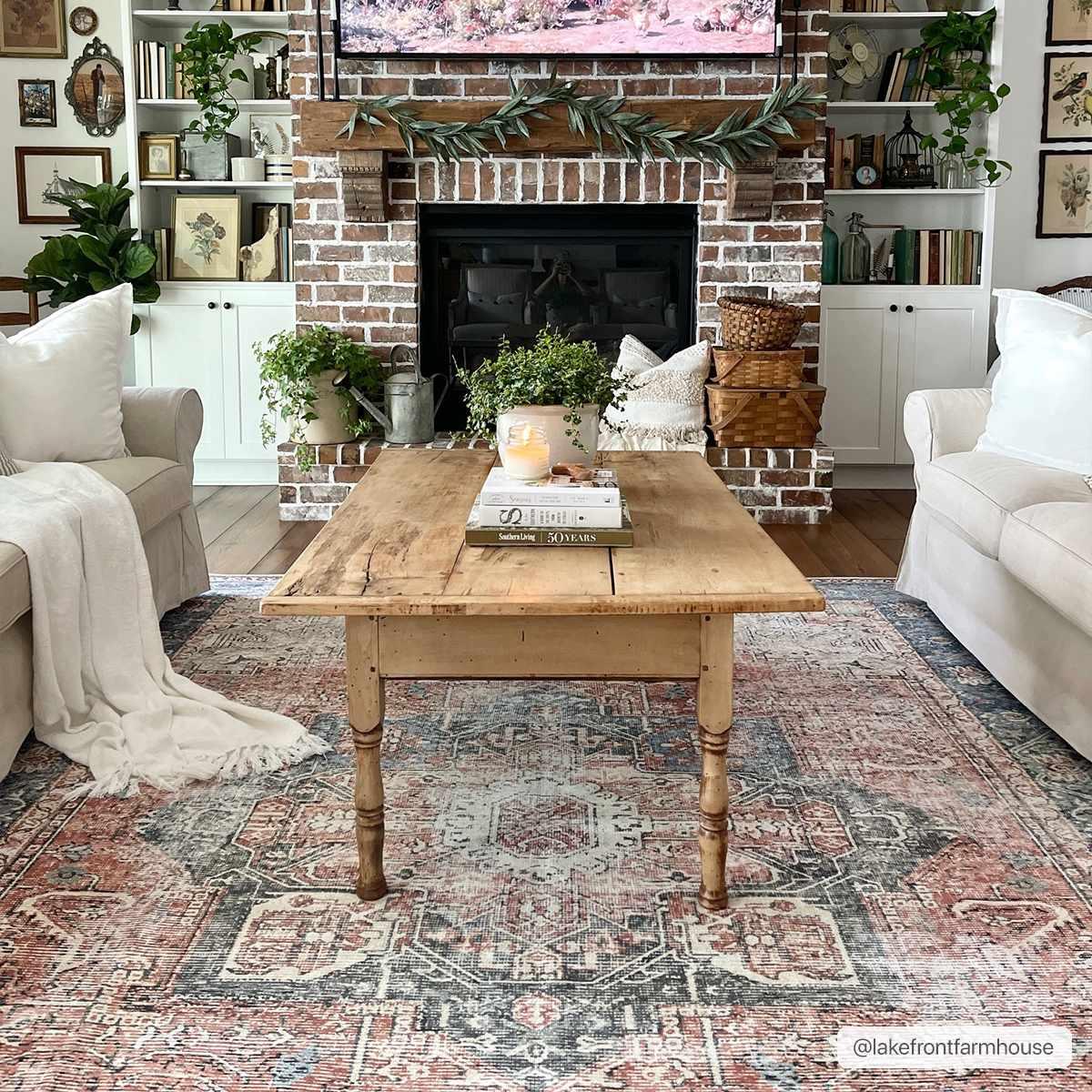 Cozy farmhouse living room with rustic coffee table, brick fireplace, and vintage rug