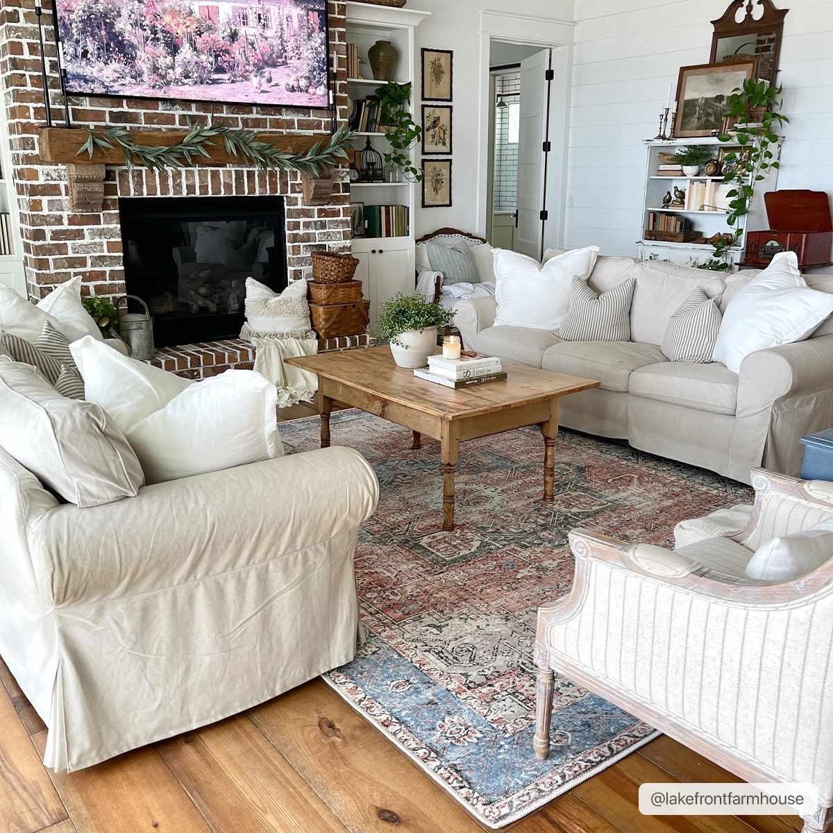 Cozy farmhouse living room with slipcovered sofas, brick fireplace, wooden coffee table, and vintage rug