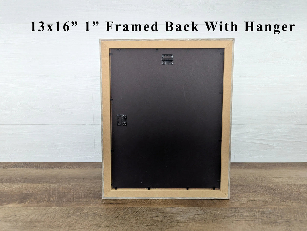 Wooden picture frame with black backing on a wooden floor against a white wall.