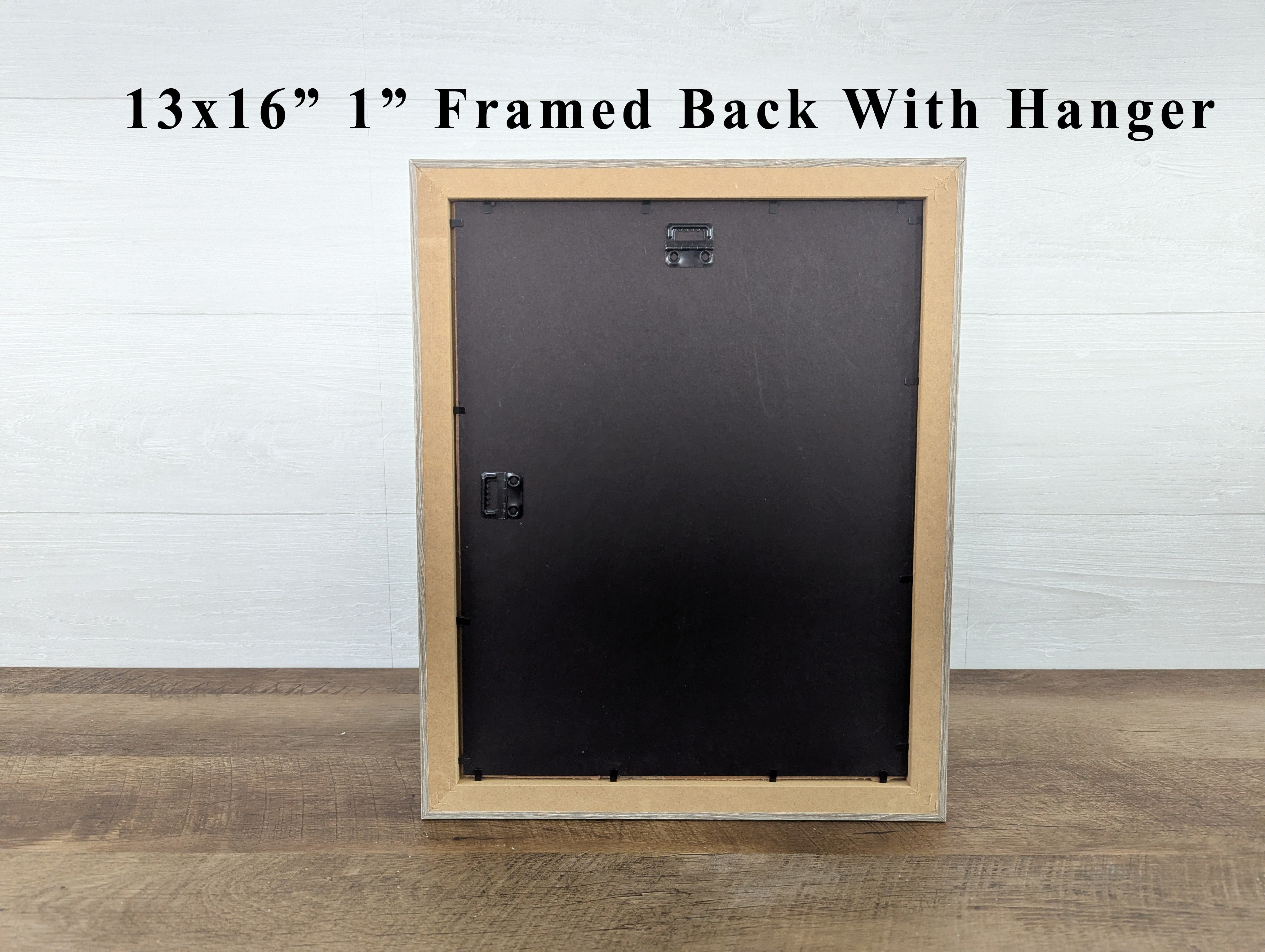 Wooden picture frame with black backing on a wooden floor against a white wall.