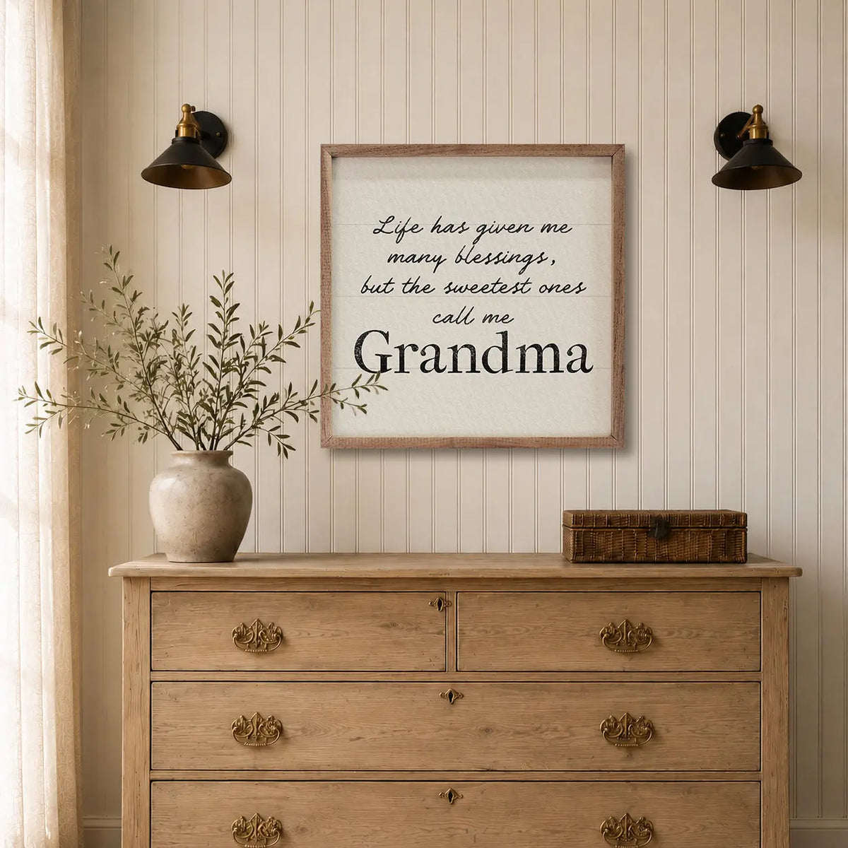 A framed typographic wall art print reading 'Life has given me many blessings, but the sweetest ones call me Grandpa' hangs on a cream paneled wall above a light wood dresser with a vase and box in a styled room.