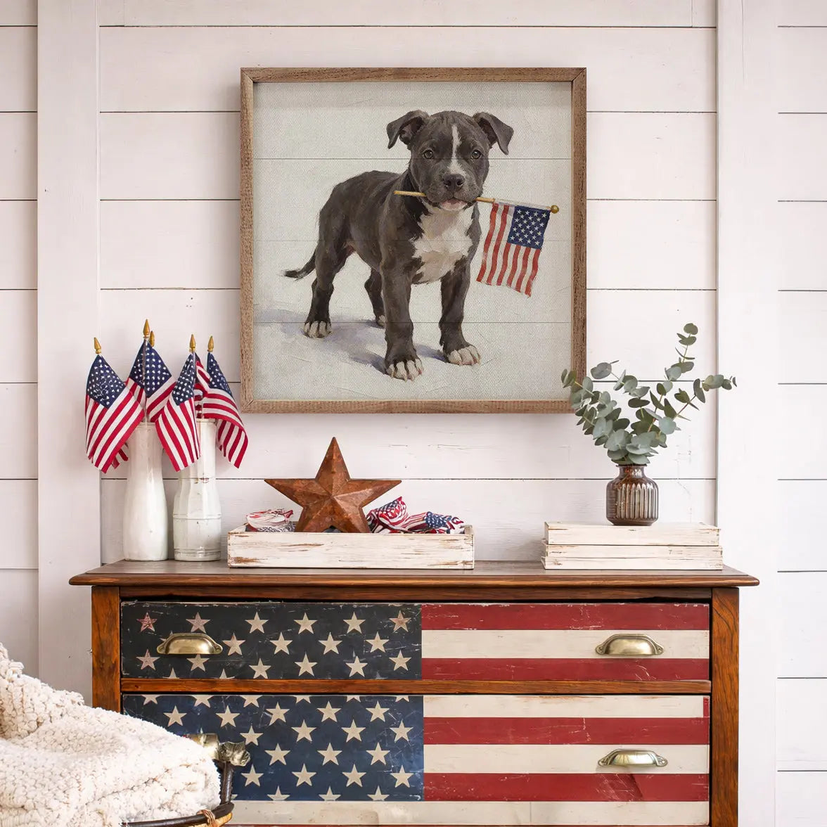 Wooden dresser with American flag design, framed picture of a dog, and small American flags on a white wall.