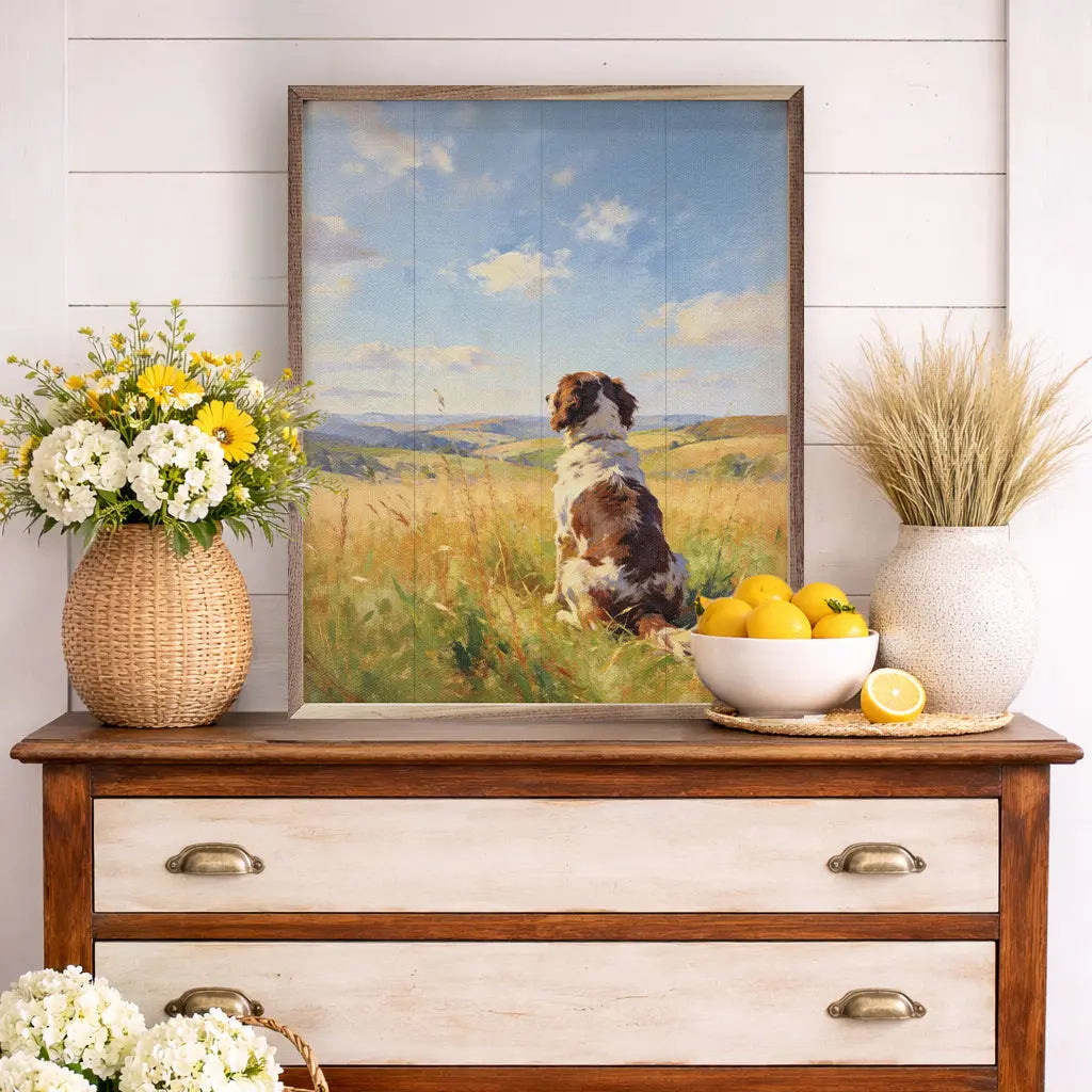 Framed painting of a dog in a field on a wooden dresser with decorative items.