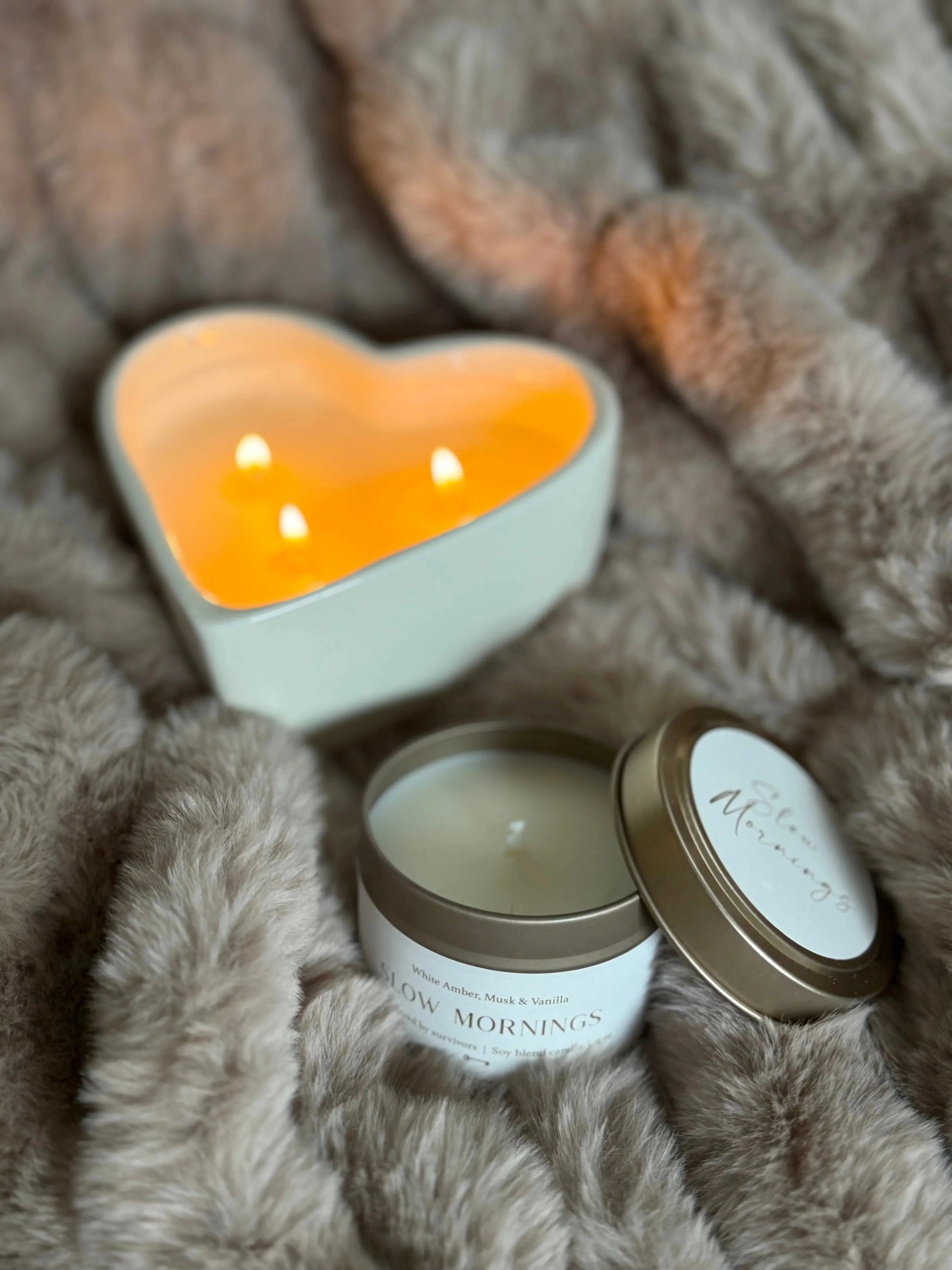 Heart-shaped candle and Slow Mornings soy candle on cozy faux fur, perfect for farmhouse home decor and relaxation.