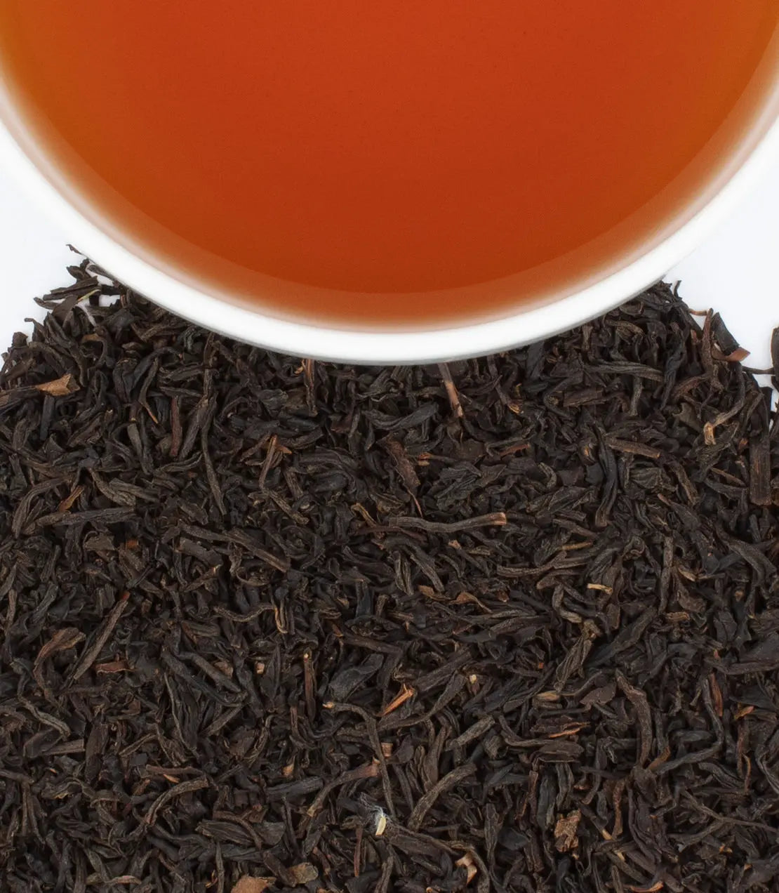 Close-up of black tea leaves with a cup of tea in the background