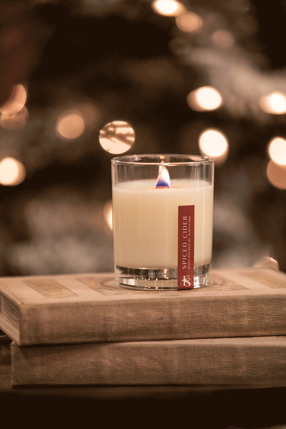 Spiced Cider candle in glass jar, lit on wooden books with cozy bokeh lights, farmhouse home decor