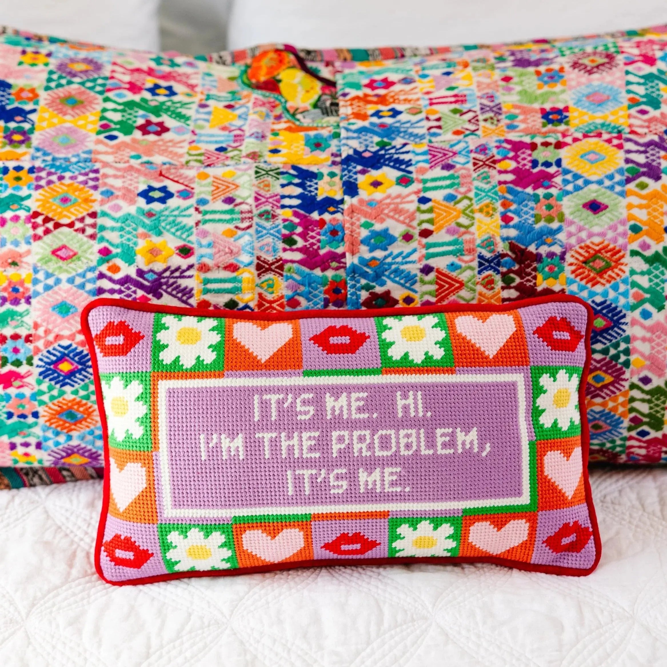 Colorful cross-stitched pillow with text and patterns on a white background